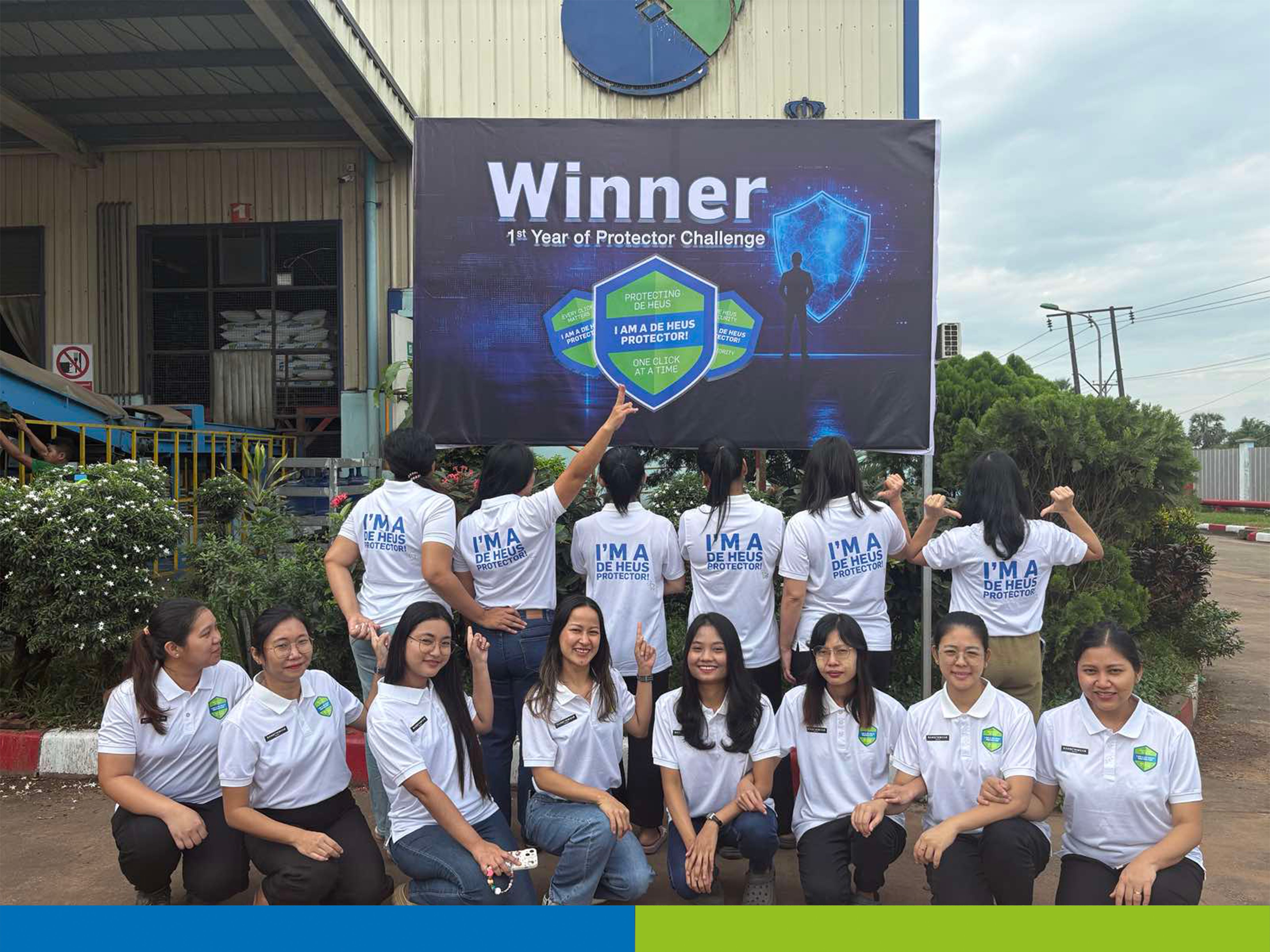 A team of De Heus employees enthusiastically celebrates winning the 'Protector Challenge' by a banner, serving as living proof of the human results of security awareness. The group proudly displays their 'I am a Protector' shirts, illustrating the successful cultural change and positive team spirit surrounding cybersecurity.